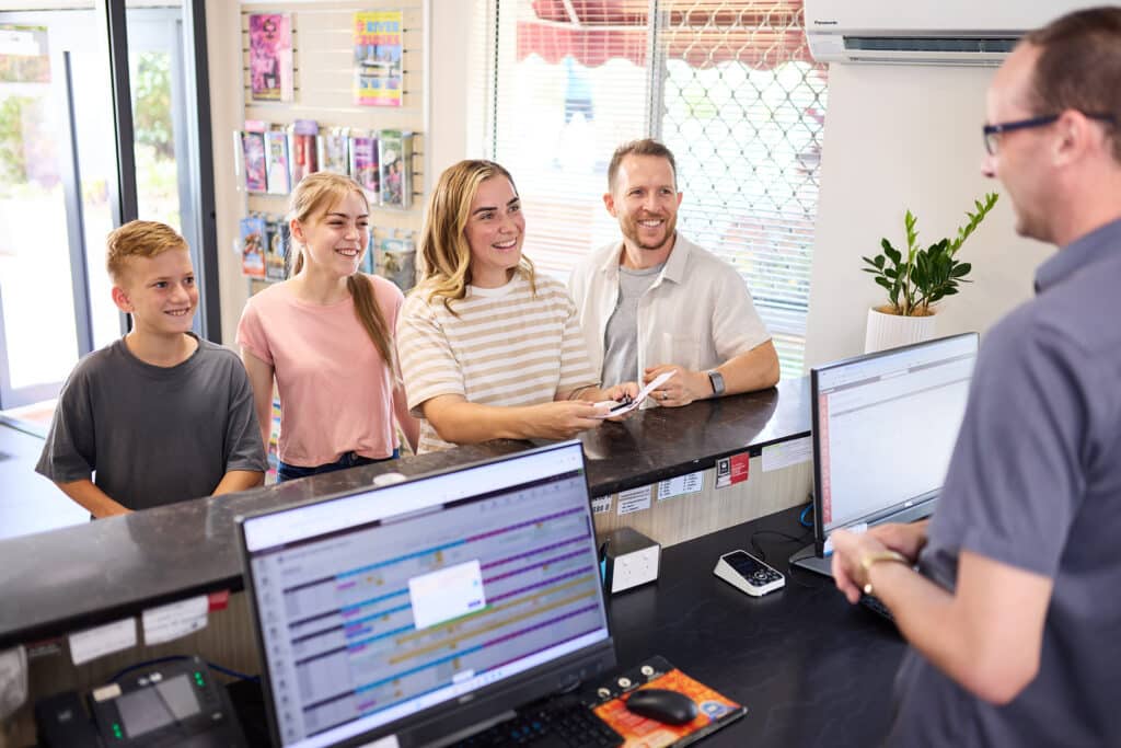 Smiling family arriving at motel reception desk meeting Guest Services Team member