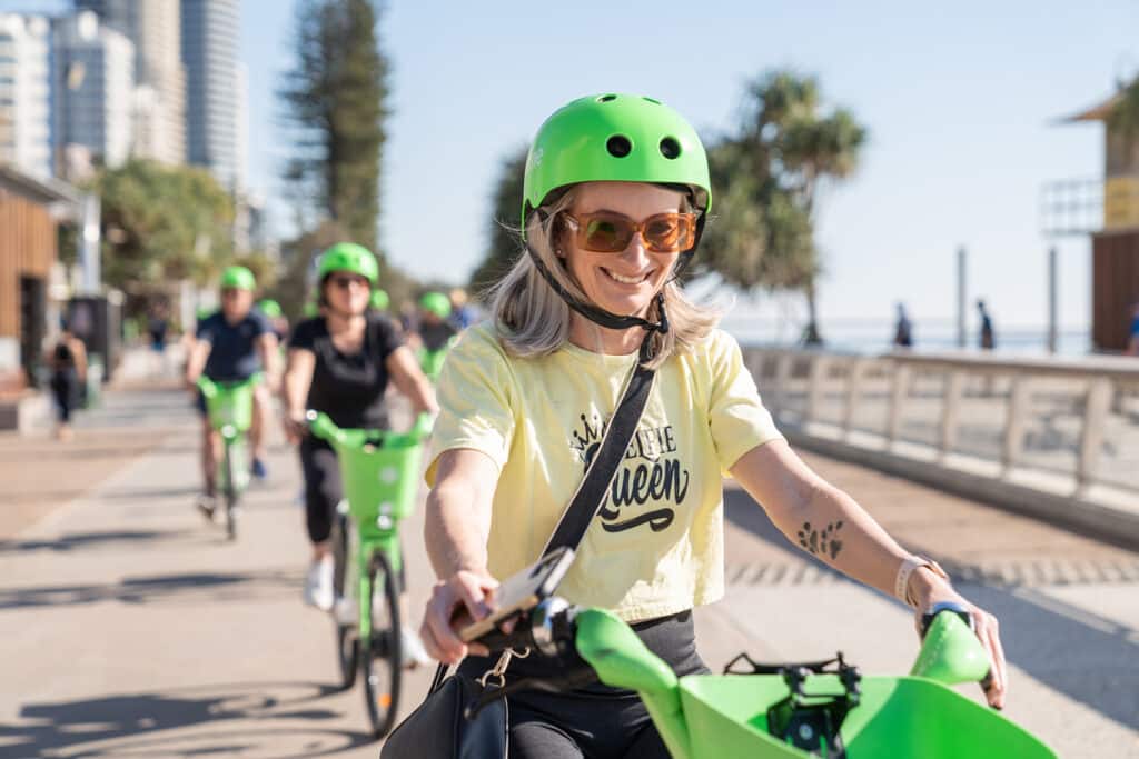 Lady riding lime bike with helmet along beach esplanade