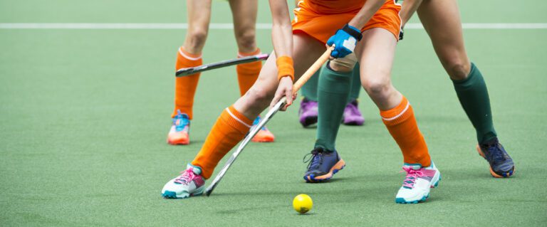 Hocky players legs, sticks and ball on green synthetic field.