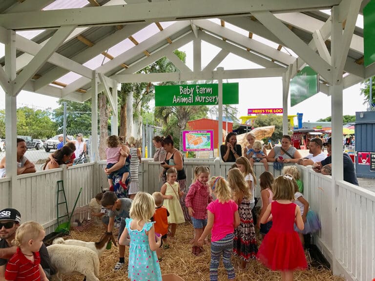 Children playing with baby animals inside white fence. Baby Farm Animal Nursery sign hanging above.