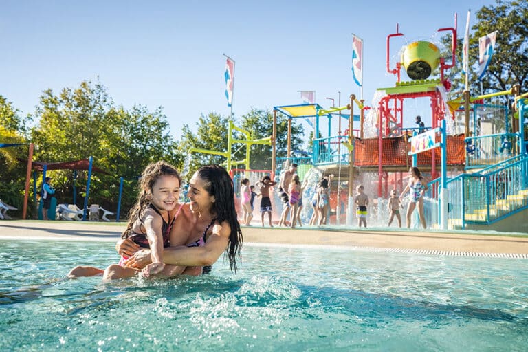 Mother and daughter in pool with water park in background